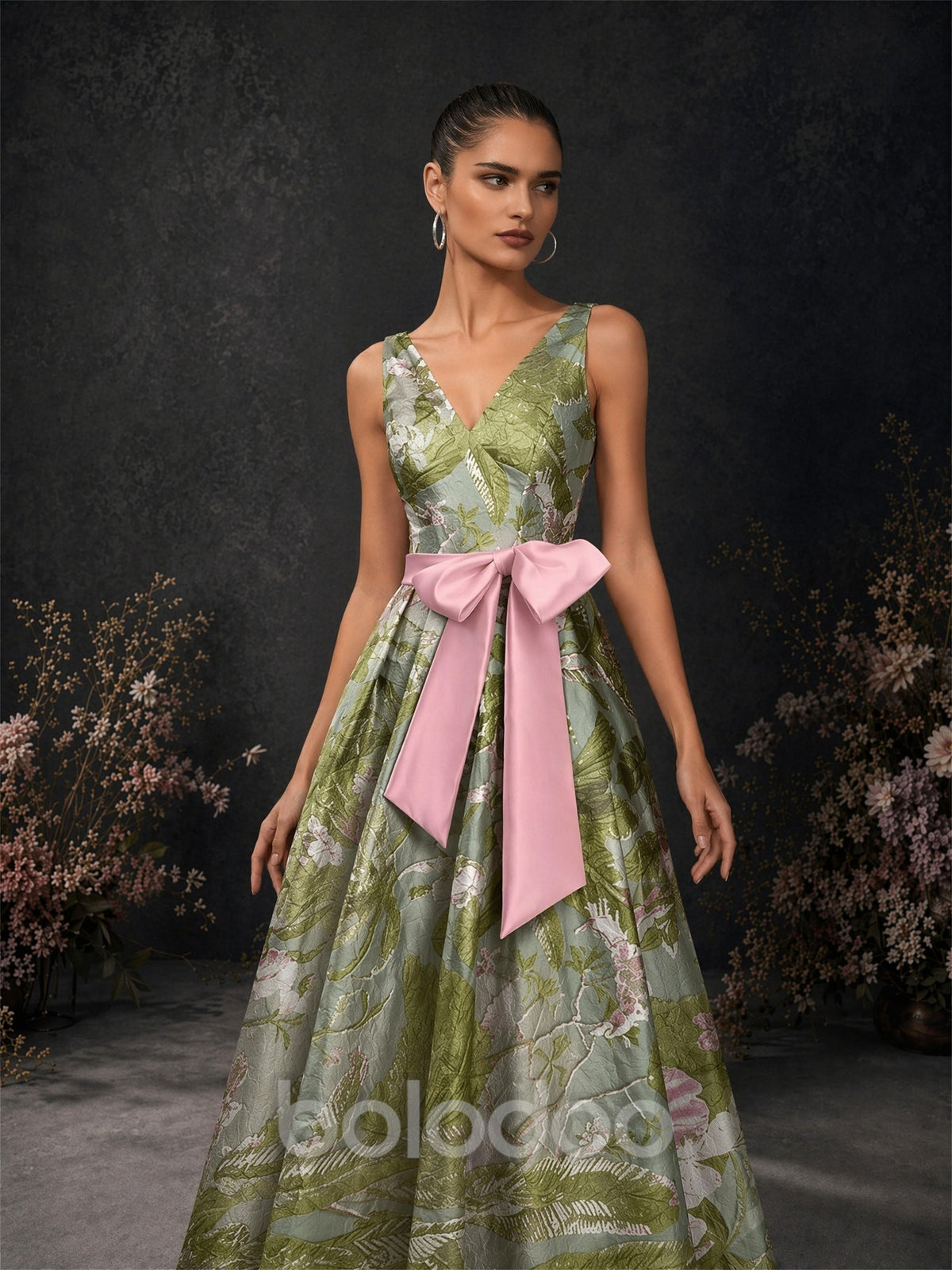 BOLODOO olive green tropical floral brocade deep V-neck dress close-up front view showing V-neckline wide straps and pink satin oversized bow belt detail | BOLODOO watermark
