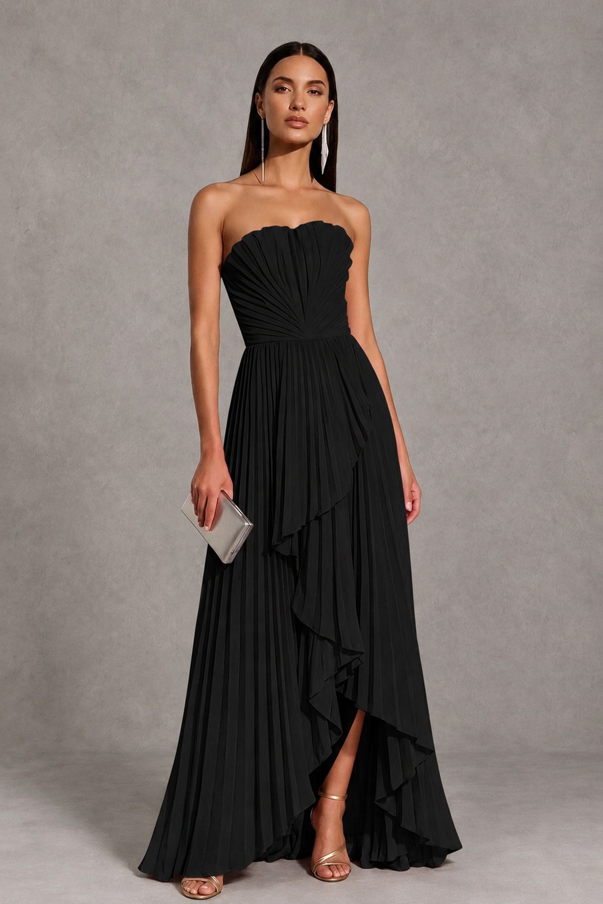 Angled front view of black strapless evening gown with pleated skirt and high-low ruffle hem