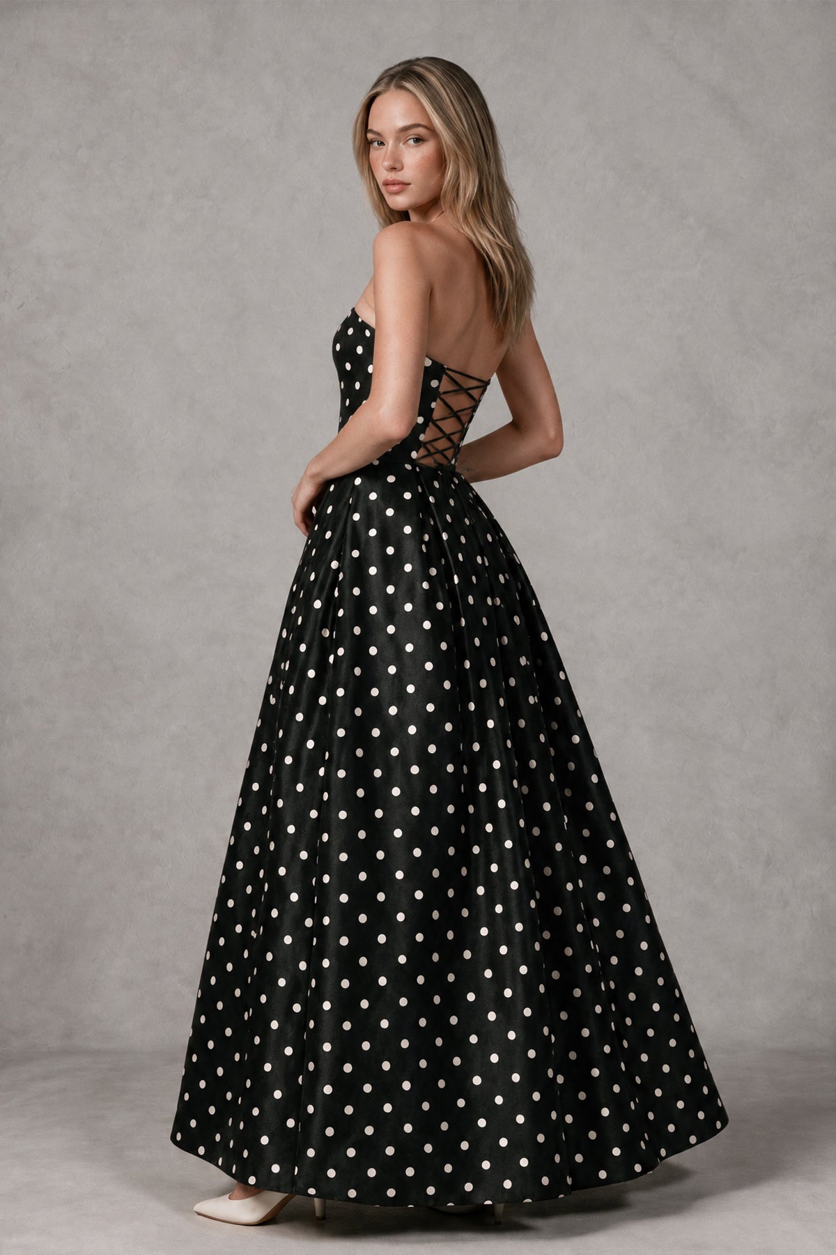 Rear three-quarter view of BOLODOO black polka dot strapless gown showing open lace-up back
