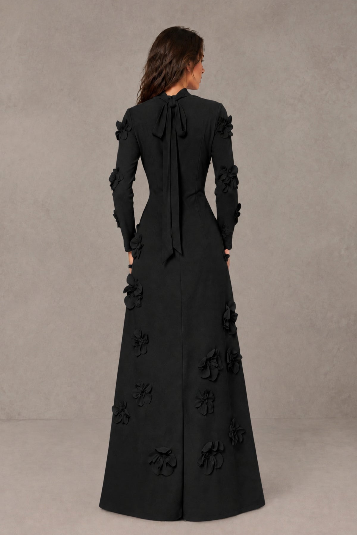 Back view of BOLODOO black high-neck floral evening gown showing covered back and long bow ribbon detail