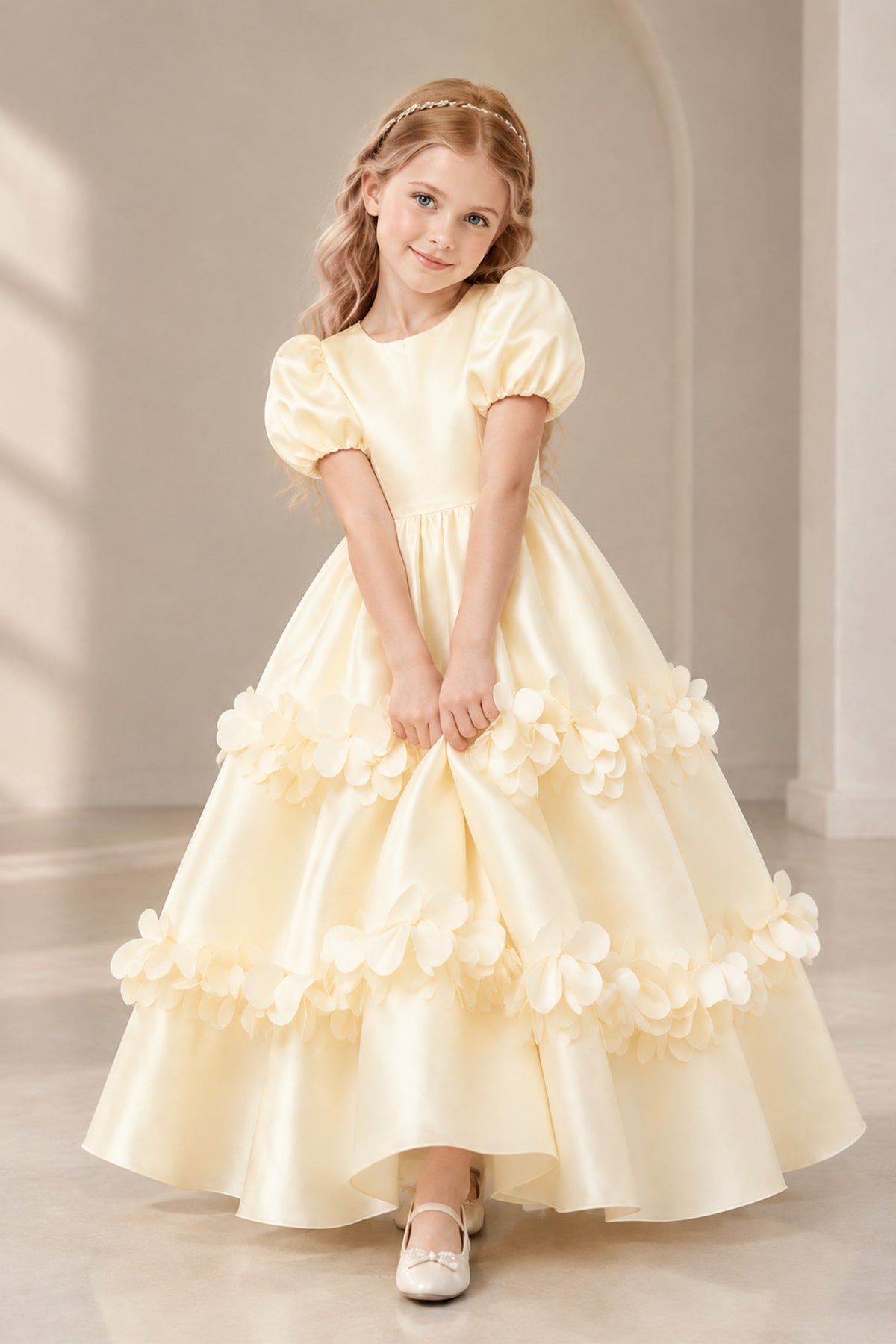 Front view of a girl wearing a champagne satin flower girl dress with puff sleeves and tiered floral appliques