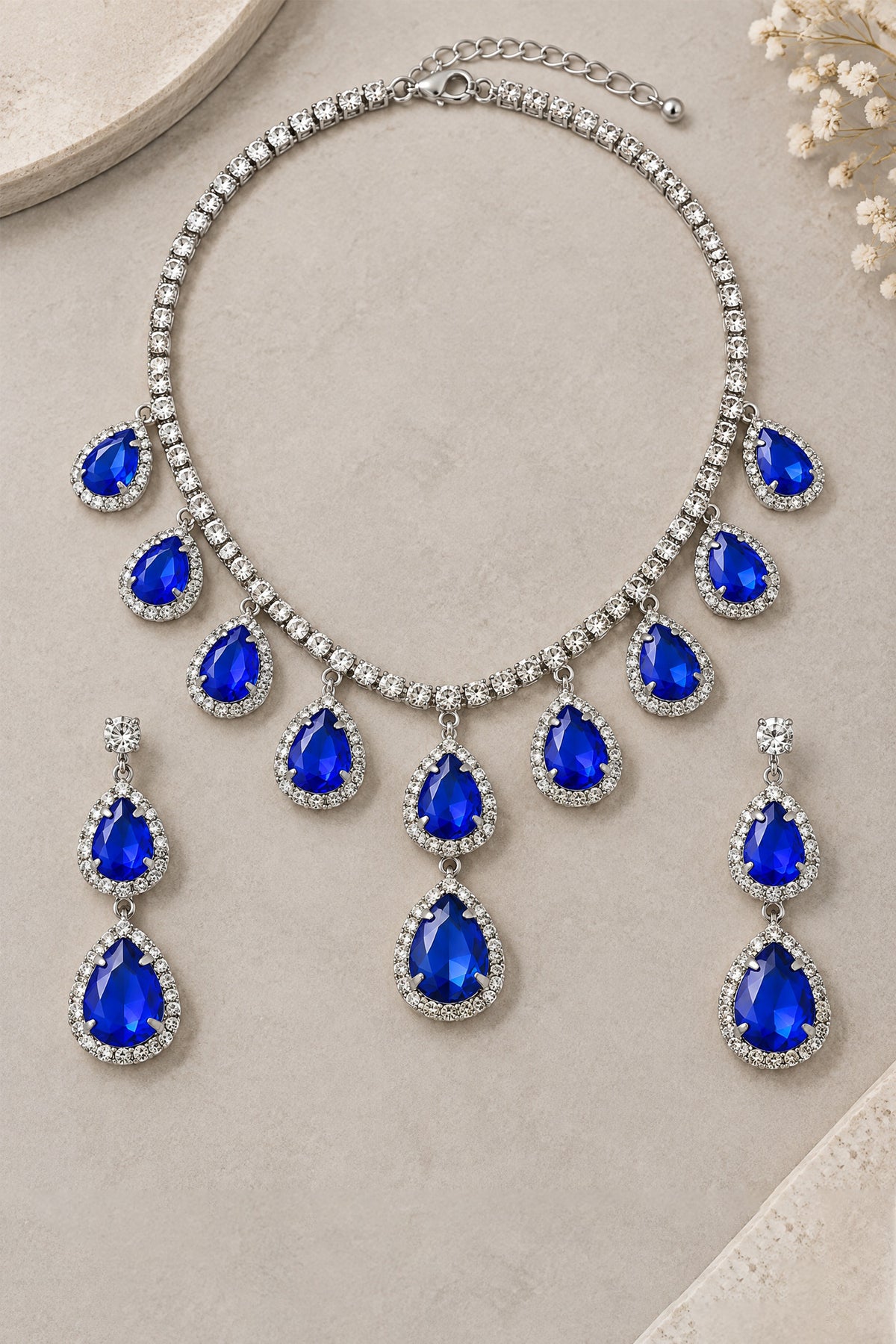 BOLODOO royal blue teardrop necklace and matching drop earrings set with silver-tone halo detailing, flat lay