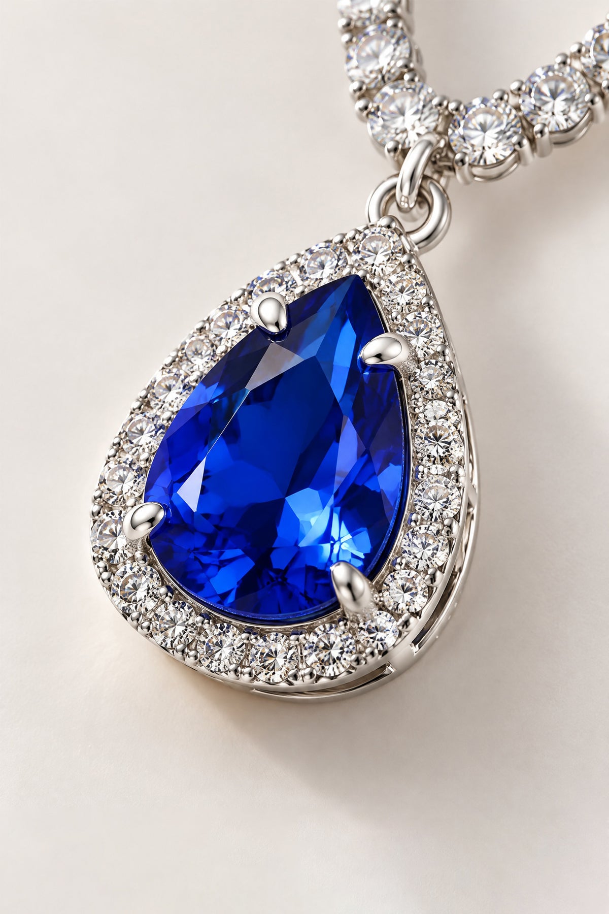 Close-up of a faceted royal blue teardrop pendant framed by clear halo accents in a silver-tone setting