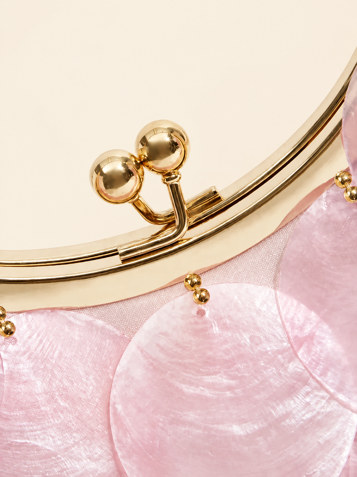 Close-up of the gold kiss-lock clasp and pink disc detail of the evening bag